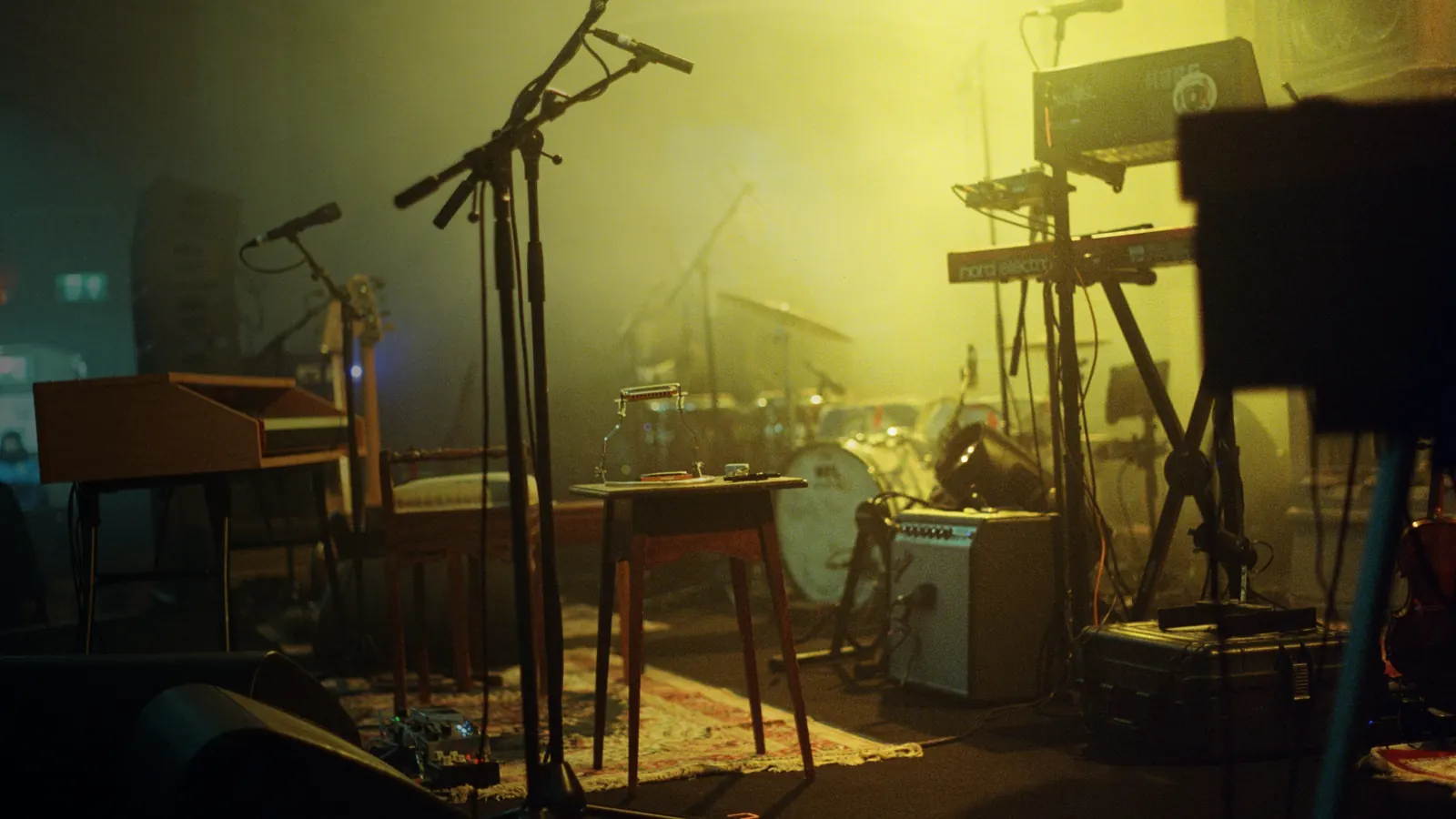 A stage set up with keyboards, mic stands and a drum kit under hazy yellow light, nobody on it yet