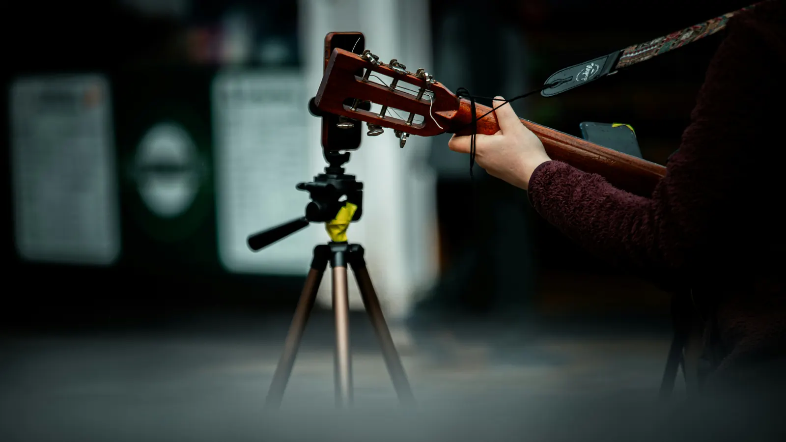 A guitar being played to a phone on a tripod in a dark room