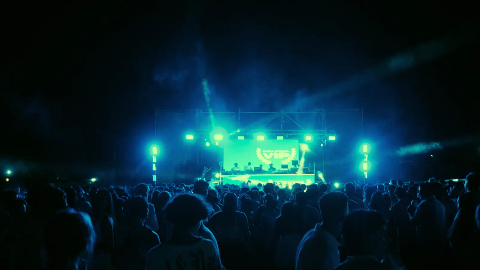 A large night crowd at an open-air festival, facing a lit stage