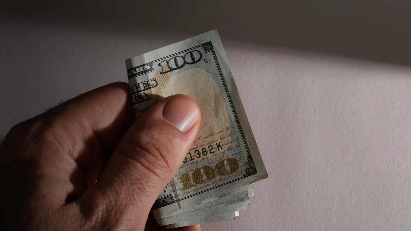 A hand holding a fan of hundred-dollar bills against a dark background
